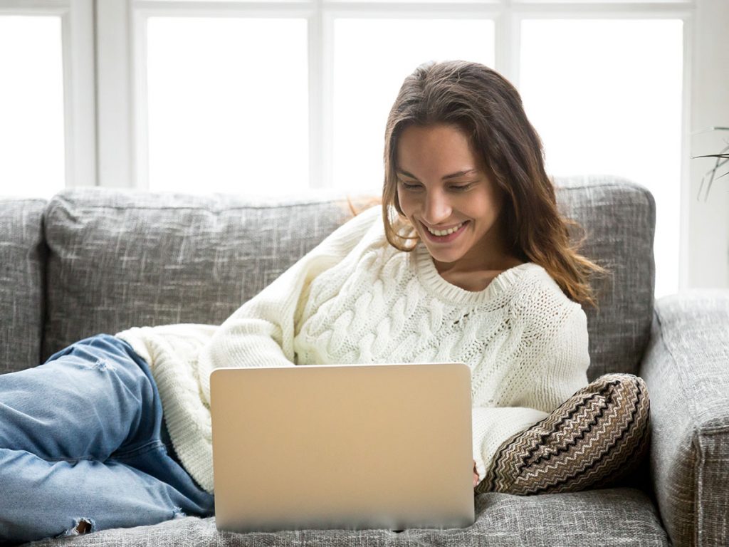 LiveChats WordPress mujer acostada en su sofa viendo su ordenador, mujer vestida con jersey blanco